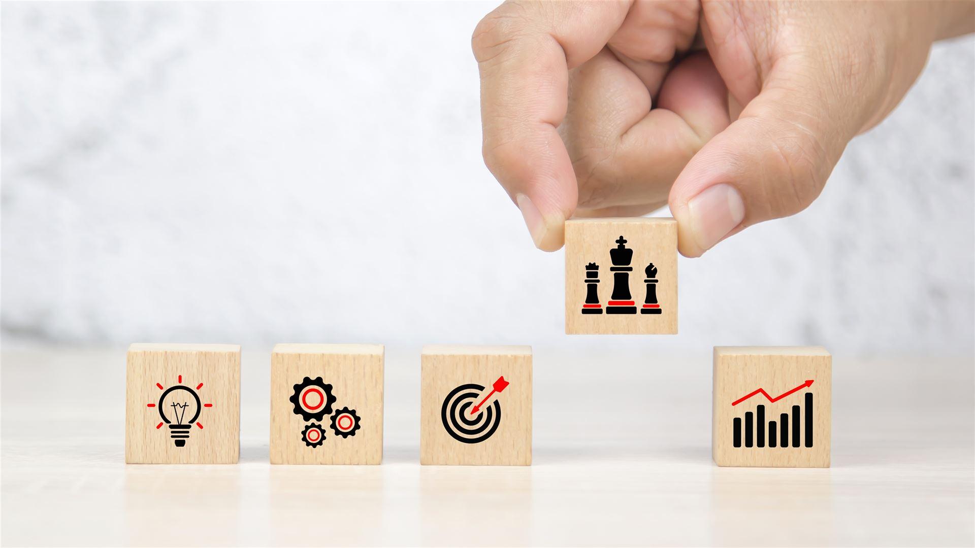 Holzbausteine mit Symbolen für Idee, Prozess, Ziel, Strategie und Wachstum – symbolisieren die Entwicklung und Umsetzung einer erfolgreichen HR-Strategie