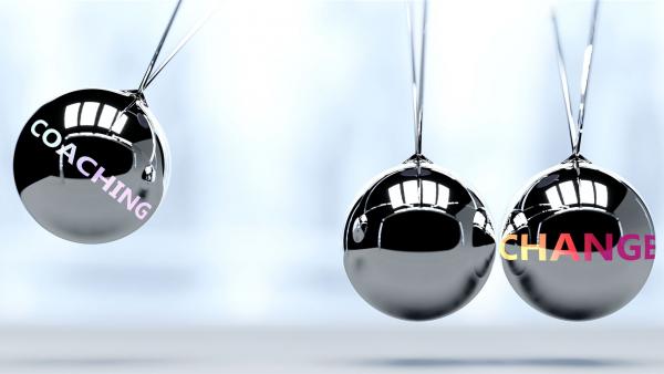 Silberne Pendelkugeln mit den Wörtern 'Coaching' und 'Change' symbolisieren Impulse für Veränderung durch professionelles Executive Coaching