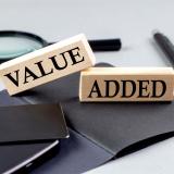 Holzblöcke mit der Aufschrift 'Value Added' auf Schreibtisch mit Notizbuch, Stift und Lupe – symbolisiert den Mehrwert professioneller Beratung durch Kienast Leadership Consulting